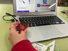 Student demonstrates the Butterfly project holding a micro:bit in one hand and showing the code on their computer screen. 